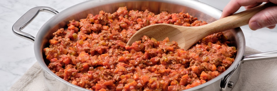 someone stirring ragu bolognese in skillet